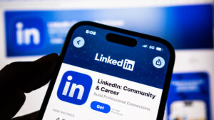 Closeup of a hand holding a smartphone displaying the linkedin app store page on a blurred background